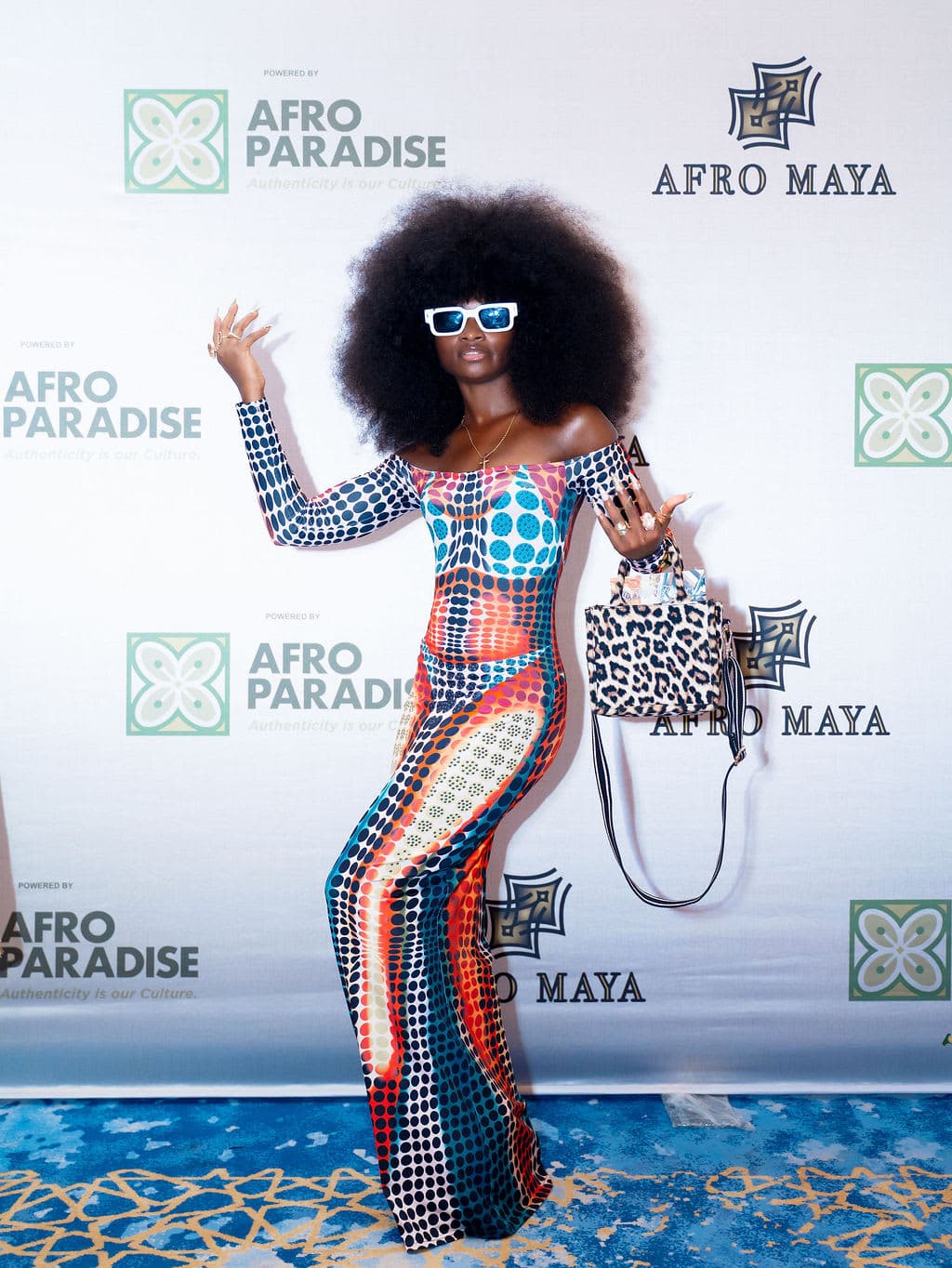 A guest poses in front of the AfroMaya–AfroParadise photography backdrop